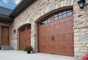 Lovely arched wood garage doors with two windows in each, installed on a stonework-covered house.